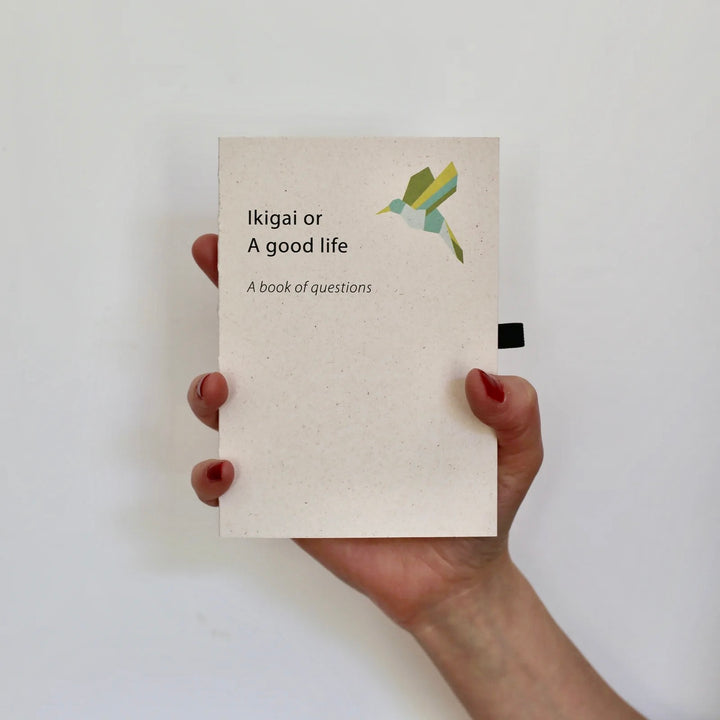 Hand holding English version of 'Ikigai or A Good Life - A Book of Questions,' a minimalistic journal encouraging self-reflection and mindfulness.