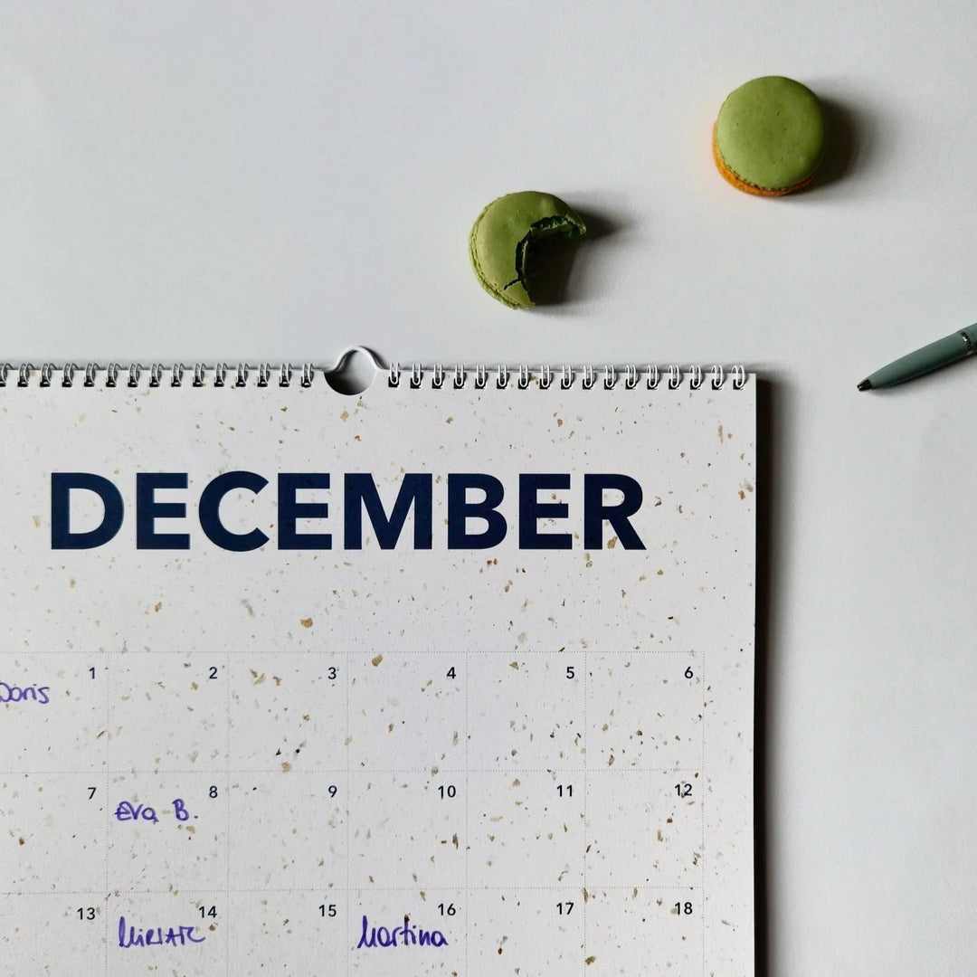 December page of the everlasting calendar with handwritten names, a green macaron, and a pen on the side.