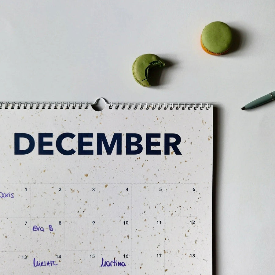 December page of the everlasting calendar with handwritten names, a green macaron, and a pen on the side.