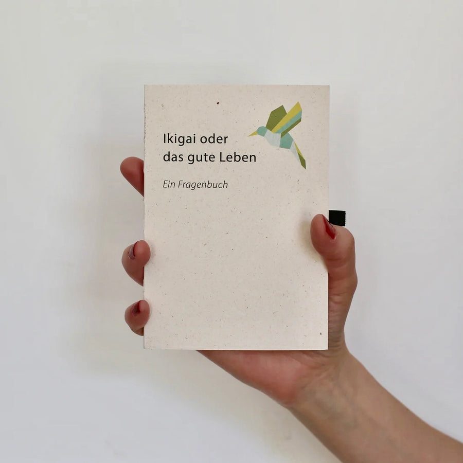 Vorderseite des Ikigai Buchs auf Deutsch, gehalten in Händen, mit Stiftschlaufe.