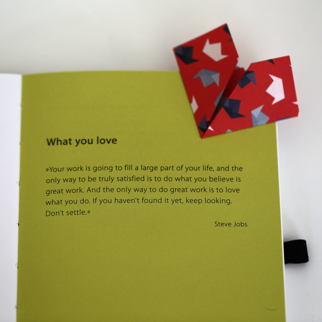 Page from Chapter 1 of the 'Ikigai or A Good Life' book featuring an inspirational quote by Steve Jobs about loving your work, with a red origami bookmark.
