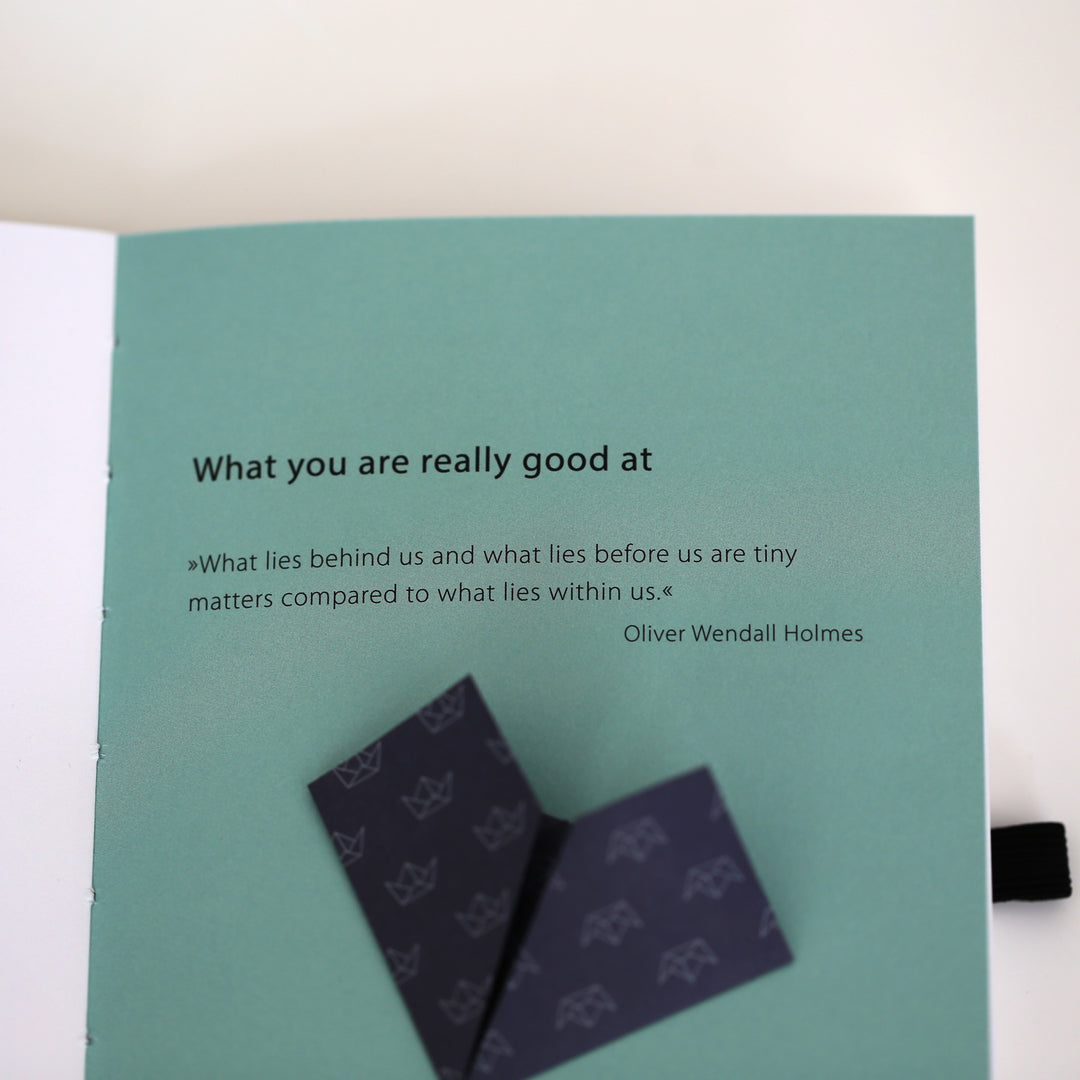 Inspirational quote from Oliver Wendell Holmes on a page from chapter 2 of the 'Ikigai or A Good Life' book, focusing on what you are really good at, accompanied by a folded paper bookmark.