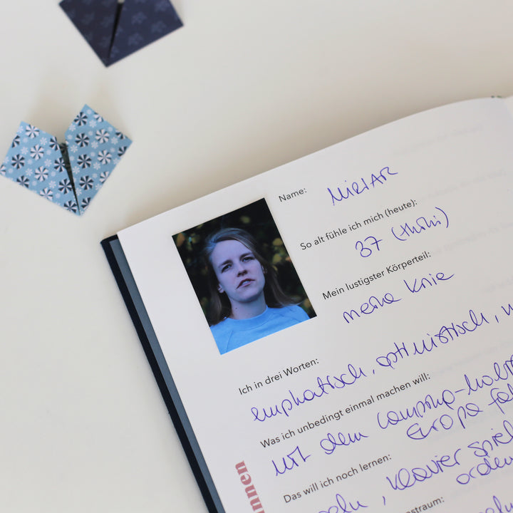 Page inside from the "Book of Friendship" showing a filled personal entry with a photo, name, and handwritten responses, surrounded by folded paper hearts. 