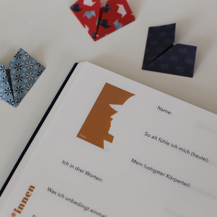 Open page from the "Book of Friendship" showing a personal yellow profile section with prompts for name, age, personality traits, and a space for a photo, surrounded by folded paper hearts.