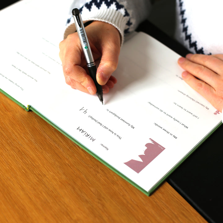 Person filling out a friendship book page with a pen, writing in the 'This is how old I feel' section.